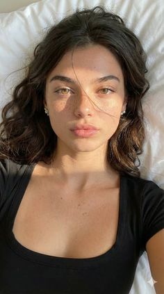 Woman with freckles and long brown hair wearing a black top, lit by soft sunlight