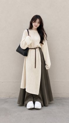 Woman in a cream sweater dress with a brown belt and black shoulder bag