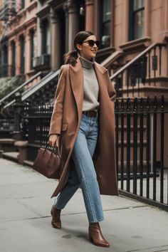 Woman in a long brown coat and jeans walking on a city street