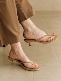 Person wearing brown pants and kitten heel flip flops on a tiled floor