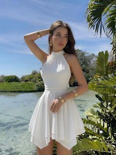 Woman in a white dress and gold jewelry posing by clear water outdoors