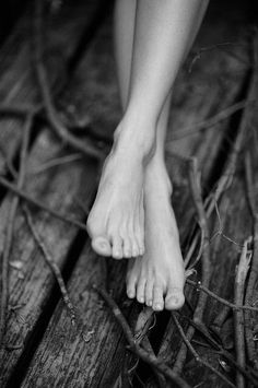 Bare feet with crossed legs on wooden planks and twigs in black and white