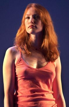 Woman with red hair in an orange tank top against a dark background