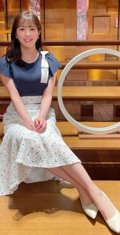 Woman with long hair wearing a blue top and white skirt, sitting indoors