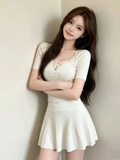 Woman with long brown hair wearing a white top and pleated skirt, arms crossed