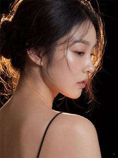 Woman with dark hair in an updo, lit by a warm backlight against a dark background