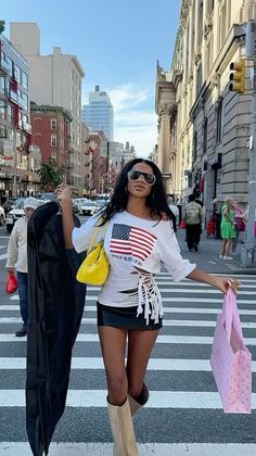Woman in a mini skirt and crop top crossing a city street with shopping bags