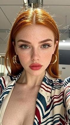 Woman with red hair and freckles wearing a striped shirt and gold hoop earrings