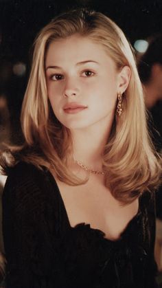 Blonde woman with long hair wearing a black top and jewelry