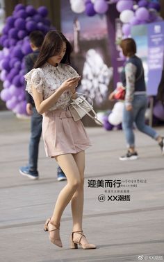 Woman in a floral shirt and pink shorts walking outdoors while looking at her phone