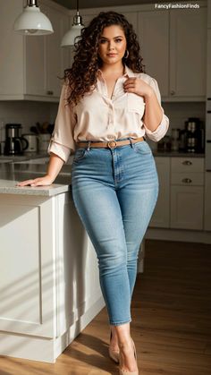 Woman with curly long hair wearing a blouse and jeans in a kitchen