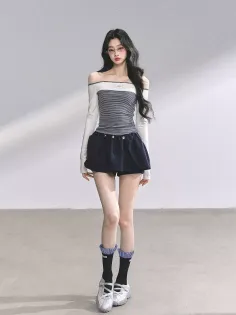 Woman with long dark hair wearing an off-shoulder top and puffy shorts indoors