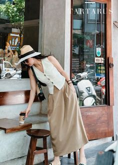 Woman in a straw hat and long skirt reaching for a coffee cup outdoors
