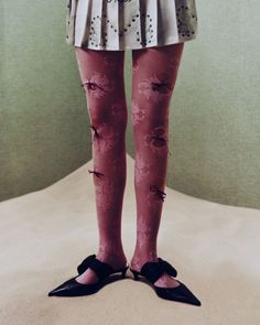 Lower body of a person wearing pink lace tights with bows and black kitten heels