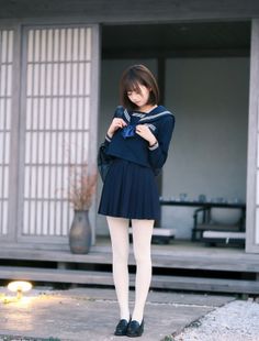 Woman in a school uniform with a pleated skirt and white tights outdoors