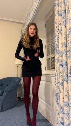 Woman in a black dress and red tights standing indoors