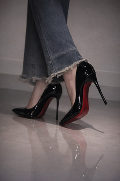 Person wearing black high heels with red soles and frayed denim jeans
