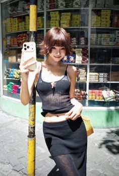 Woman in a sheer black top taking a selfie on a sunny street