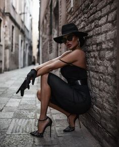 Woman in a black dress, hat, and sunglasses posing in an alleyway