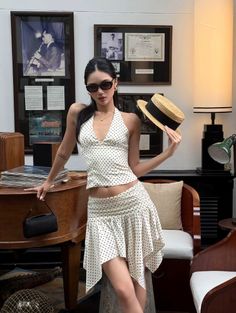 Woman in a polka dot halter top and mini skirt holding a straw hat indoors