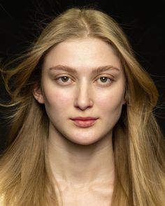 Close-up portrait of a woman with blonde hair and green eyes against a dark background