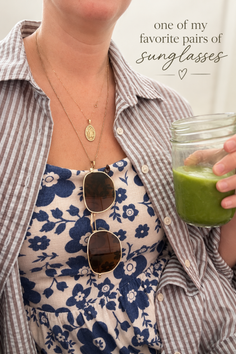 Person wearing a striped shirt over a floral dress, holding a green smoothie