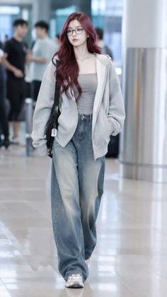 Woman with long red hair and glasses wearing a gray hoodie and baggy jeans indoors