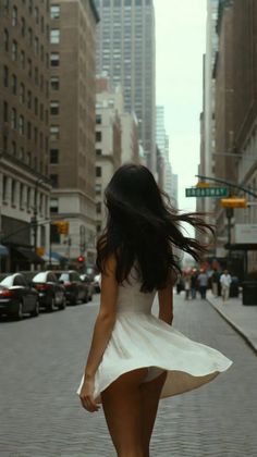 Woman in a white dress with hair blowing, walking down a city street