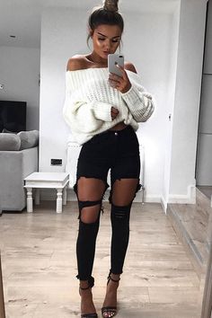 Woman in an off-shoulder sweater and ripped jeans taking a mirror selfie