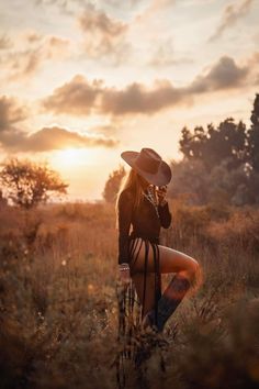 Woman in a cowboy hat and revealing outfit posing in a field at sunset