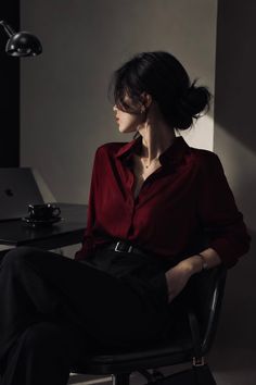 Woman in a red shirt and black pants sitting indoors with dramatic lighting