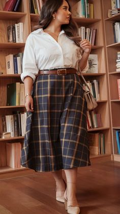 Woman in a white shirt and plaid skirt standing in front of bookshelves