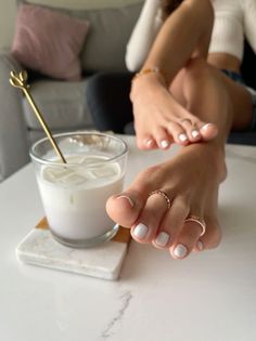 Woman's bare feet with white pedicure and toe rings next to a drink