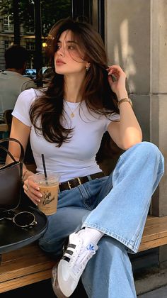 Woman with long brown hair in a white t-shirt and jeans at an outdoor cafe