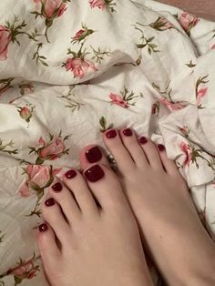 Feet with red nail polish on floral patterned bed sheets
