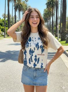 Smiling woman with long hair wearing a t-shirt and denim skirt on a street with palm trees