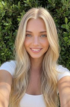 Blonde woman with blue eyes and freckles smiling in front of green foliage