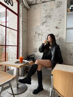 Woman in a leather jacket and knee-high boots drinking in a cafe