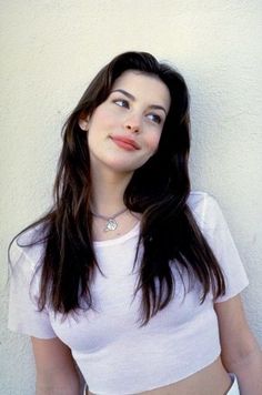 Woman with long dark hair wearing a pink crop top and choker against a light wall