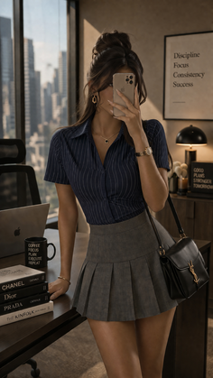 Woman in a striped shirt and pleated skirt taking a mirror selfie in an office