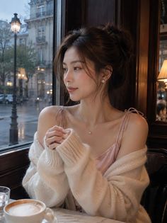 Woman in a cafe wearing a pink top and cardigan, looking out a window