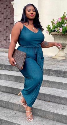 Woman in a teal jumpsuit and heeled sandals standing on outdoor stairs