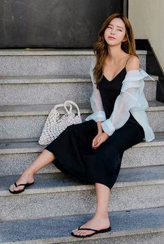 Woman in a black dress and sheer top sitting on outdoor stairs