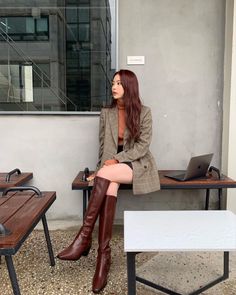 Woman in a plaid blazer and brown boots sitting outdoors with a laptop