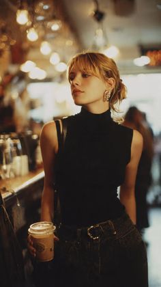 Woman with blonde hair and a black turtleneck top holding a drink indoors