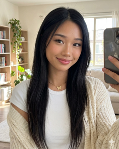 Woman with long black hair wearing a white t-shirt and cardigan indoors