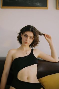 Woman in a black one-shoulder swimsuit with a cutout, pulling her hair