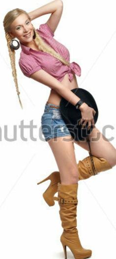 Blonde woman in a pink tied shirt, denim shorts, and cowboy boots holding a hat