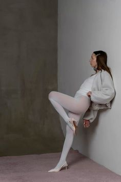 Woman in white tights and high heels leaning against a wall