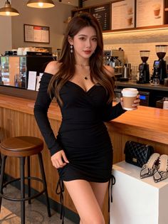 Woman in a black off-shoulder dress holding a coffee cup in a cafe